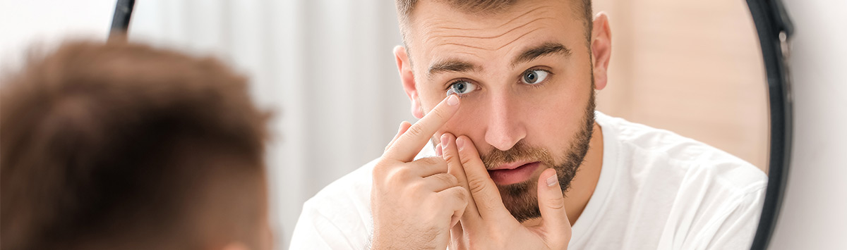 Jak założyć soczewki – młody mężczyzna zbliża palec z soczewką do oka